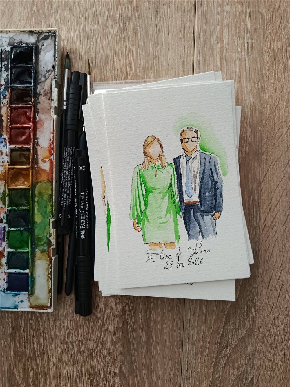 Petits portraits aquarelle des mariés réalisés en direct pour un mariage, avec palette et pinceaux